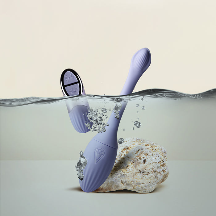 The Niya Rechargeable Kegel Exerciser and Vibrator with Remote, a purple, waterproof device, stands upright on a rock partially submerged in water, surrounded by bubbles against a plain light background.