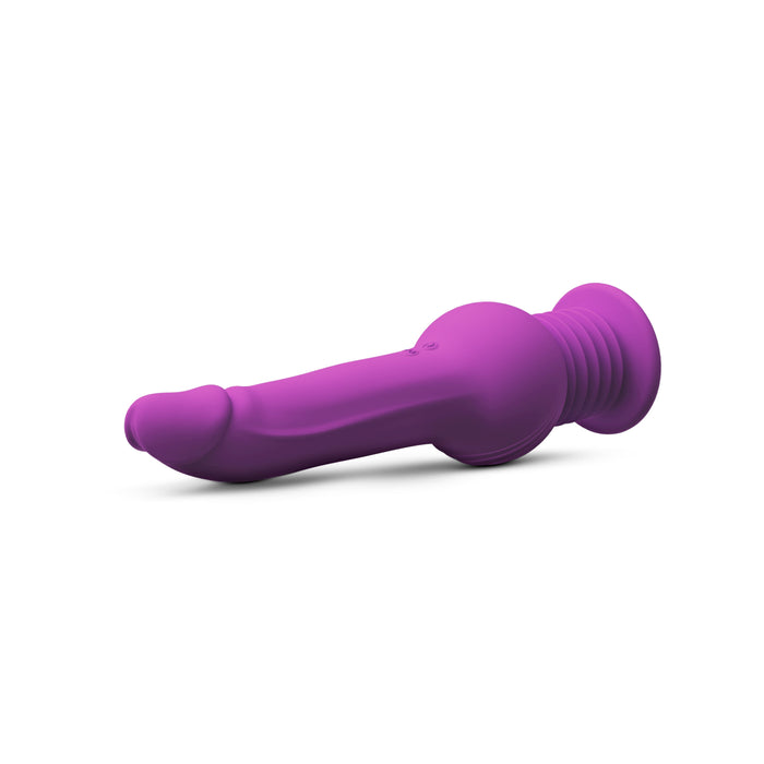 The New York Gyro Quake Thrusting 9.75 Inch Silicone Dildo - Purple by Blush, a phallic-shaped silicone plug in vibrant purple with a flared, ribbed base for safe use, is lying on its side against a white background. The toy features multiple vibrating modes for enhanced pleasure.