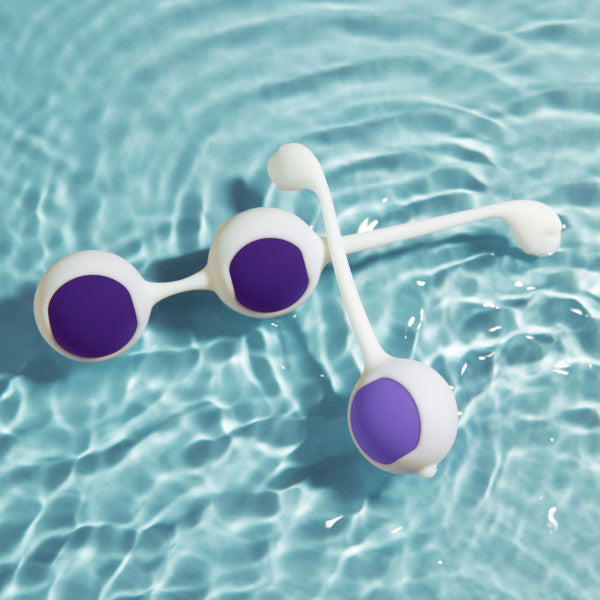 Two white and purple kegel balls from the Wellness Kegel Ball Training Kit for Pelvic Floor Health float on blue water, creating gentle ripples—an elegant reminder of strengthening your pelvic floor with this quality kit.