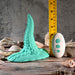 The Octopus Tentacle Insertable Remote Controlled Grinder—a teal, silicone, tentacle-shaped waterproof sex toy with suction cup details—is shown beside a measuring tape, white three-button remote, and seashells on a wooden surface.
