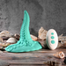 The Octopus Tentacle Insertable Remote Controlled Grinder, a turquoise waterproof sex toy, stands upright on a wooden surface among seashells with its white three-button remote placed beside it.