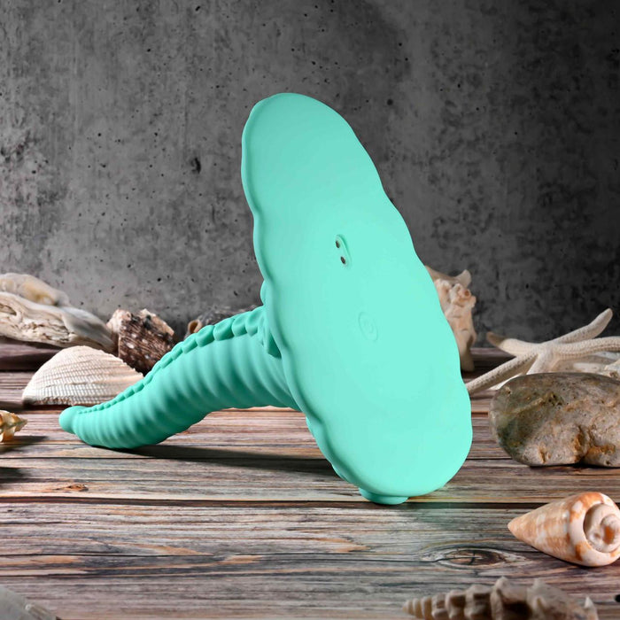 The Octopus Tentacle Insertable Remote Controlled Grinder, a turquoise silicone vibrator with a ribbed handle and cloud-shaped top, rests on wood amid seashells and coral against a textured gray wall.