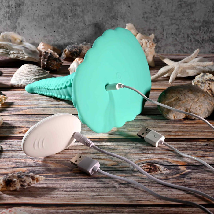 Two octopus tentacle-shaped electronic devices, one teal and one white, are plugged into USB chargers on a wooden surface with seashells—perfect for anyone seeking a waterproof, hands-free vibrator like the Octopus Tentacle Insertable Remote Controlled Grinder.