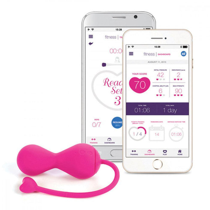 The pink OhMiBod Krush Smart Kegel Fitness Balls with a heart-shaped tail are shown next to two smartphones displaying fitness app interfaces featuring scores, time, and control options. This innovative device uses sensor technology for efficient pelvic floor training.