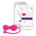 The pink OhMiBod Krush Smart Kegel Fitness Balls with a heart-shaped tail are shown next to two smartphones displaying fitness app interfaces featuring scores, time, and control options. This innovative device uses sensor technology for efficient pelvic floor training.