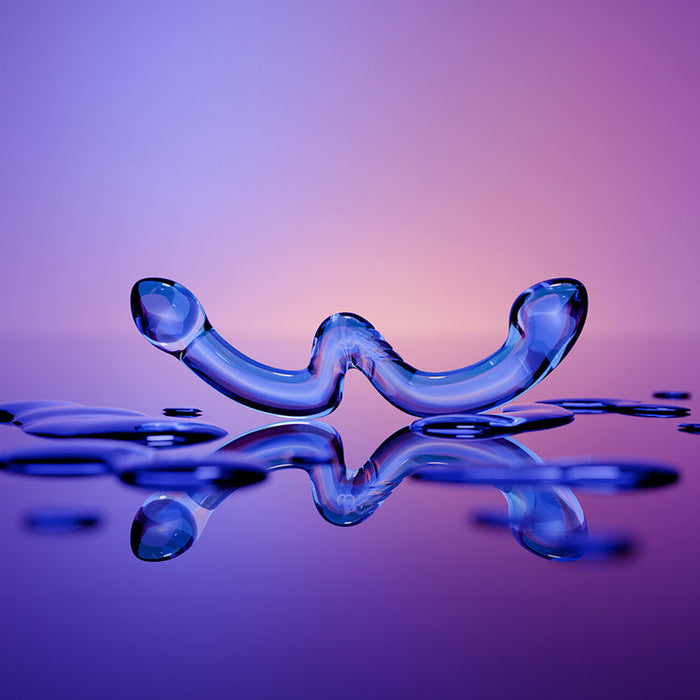 The OhWii Double-Ended Glass Dildo for G-Spot & P-Spot features a curved, abstract design with two upward-facing ends, displayed on a reflective surface with droplets against a gradient purple-orange background.