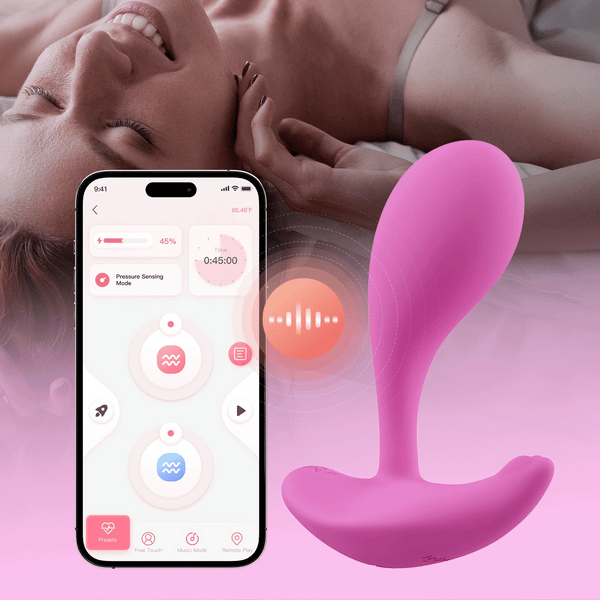 A smiling woman lies on a bed. In the foreground, an Oly 2 Pressure Sensing App-Enabled Wearable Vibrator rests beside a smartphone displaying its app-controlled, hands-free interface.
