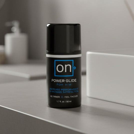 A black bottle labeled "On Power Glide for Him Penis Performance Enhancer," a male arousal gel, sits on a gray bathroom counter, with blurred toiletries and a white container in the background.