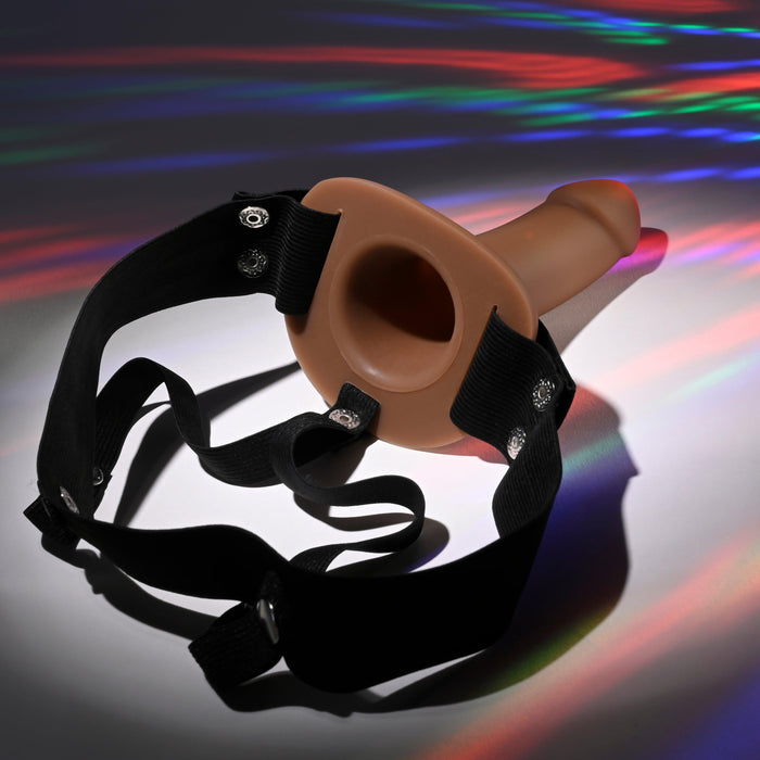 The "Our First Hollow Strap-On Dildo + Harness Set - Chocolate" features a brown, phallic-shaped strap-on with black adjustable harness straps and a flexible TPE shaft, set amidst vibrant colorful light reflections for comfort and ease of use.