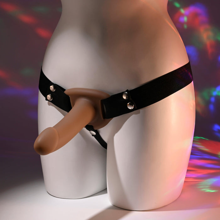 The mannequin's lower half displays the "Our First Hollow Strap-On Dildo + Harness Set - Chocolate," featuring a flexible TPE shaft that mimics real-life texture. Vibrant lighting accentuates its realistic design, ideal for beginners exploring strap-on play.