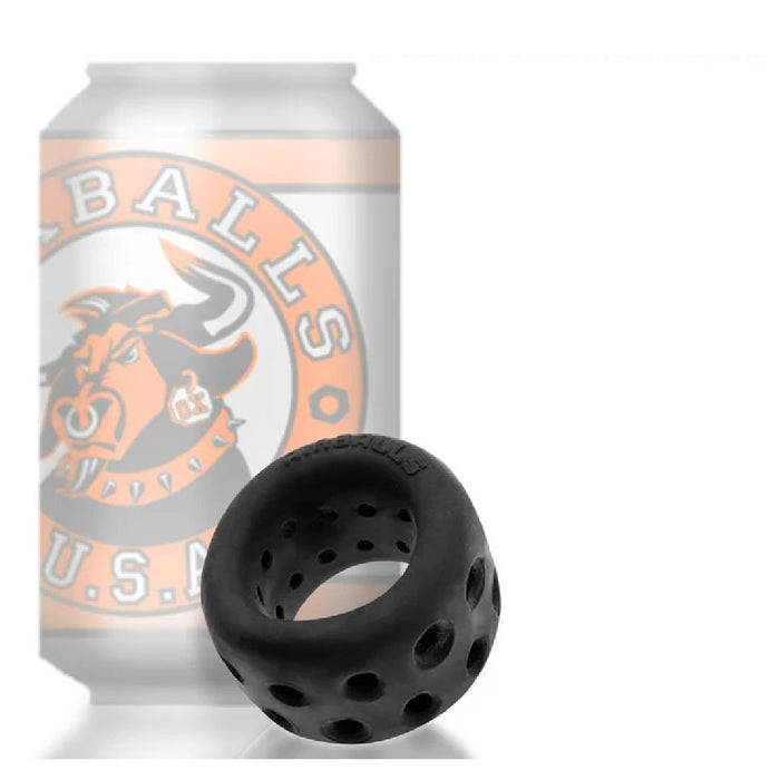 A black, perforated cylindrical object with multiple ventilation holes is placed in front of a blurred can with the logo of a raging bull and the text "BULLBALLS U.S.A." The Oxballs Air Lite Ventilated Ball Stretcher - Black Ice by Oxballs, likely made from a silicone TPR blend, features an array of circular openings throughout its surface.