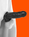 A close-up of a white sculptural figure with a black extension resembling an outstretched arm or some other protuberance, set against an orange background. The image has a surreal and abstract quality, enhanced by its Oxballs Dicker 7.5 Inch Cock Sheath - Black Ice that contours the form perfectly.
