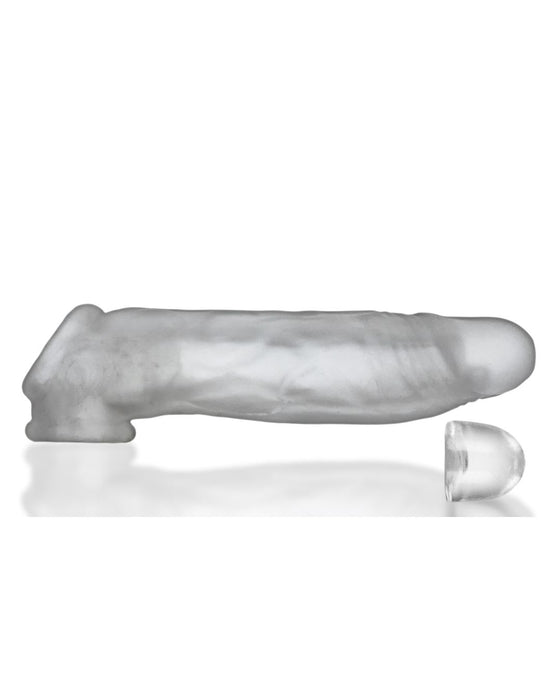 A translucent gray Oxballs Dicker 7.5 Inch Cock Sheath - Clear Ice in the shape of an erect penis, featuring textured veins and a separate detachable tip. The sleeve, designed for a slimmer fit sheath, is shown on a reflective white surface, highlighting its smooth and slightly shiny texture.