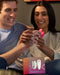 A smiling couple excitedly looking at a new touch-sensitive We-Vibe Chorus Remote & App Controlled Couples' Vibrator in Crave Coral together, holding it in their hands while sitting comfortably at home.