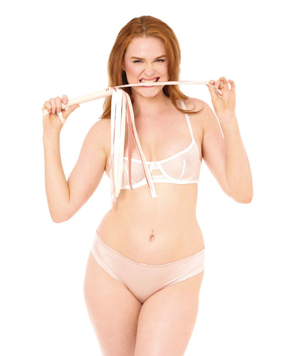 A woman with long red hair in light pink lingerie stands against a white background, smiling and playfully biting the end of the Peaches 'n Cream Flogger, which features multiple creamy faux leather straps.