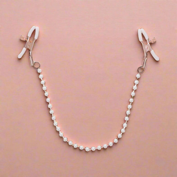 The Peaches 'n Cream Pearl Nipple Clamps by Sportsheets feature elegant nipple clamps in rose gold, linked by a string of pearl accents. Each clamp is carefully crafted with white rubber tips to enhance grip, combining both functionality and decorative appeal.