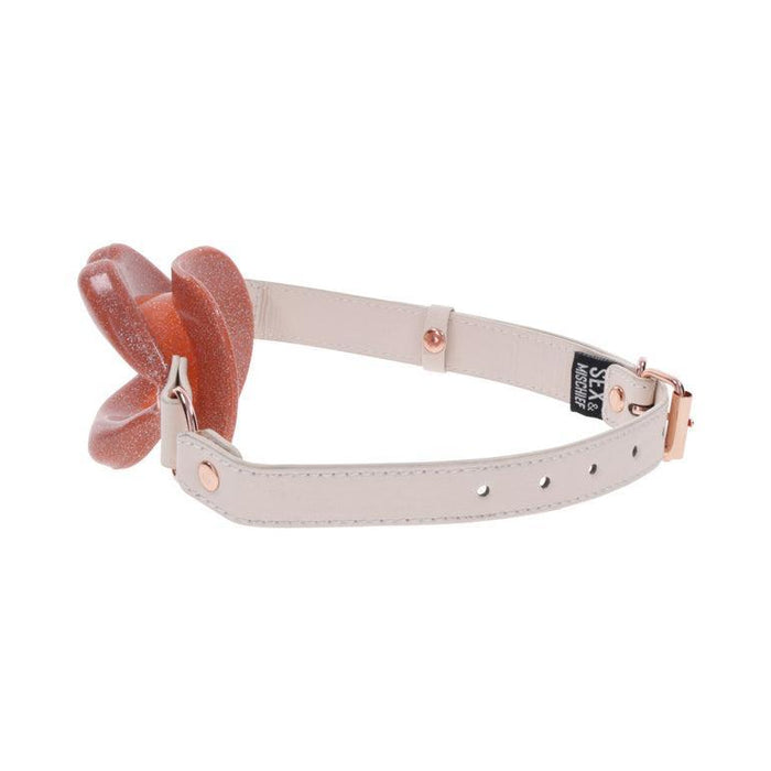 An exquisite masterpiece by Sportsheets, the Peaches 'n Cream Silicone Lips Open Mouth Gag features a beige adjustable strap with a rose gold buckle. It is adorned with a large brown flower-like ornament boasting a glittery texture, reminiscent of unique lips gag designs. Accompanied by a small black tag embossed with white text, this piece truly stands out.