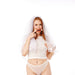 A woman in white bridal lingerie and a veil stands against a white backdrop, playfully holding the Peaches 'n Cream Silicone Lips Open Mouth Gag to her face with a mischievous look.