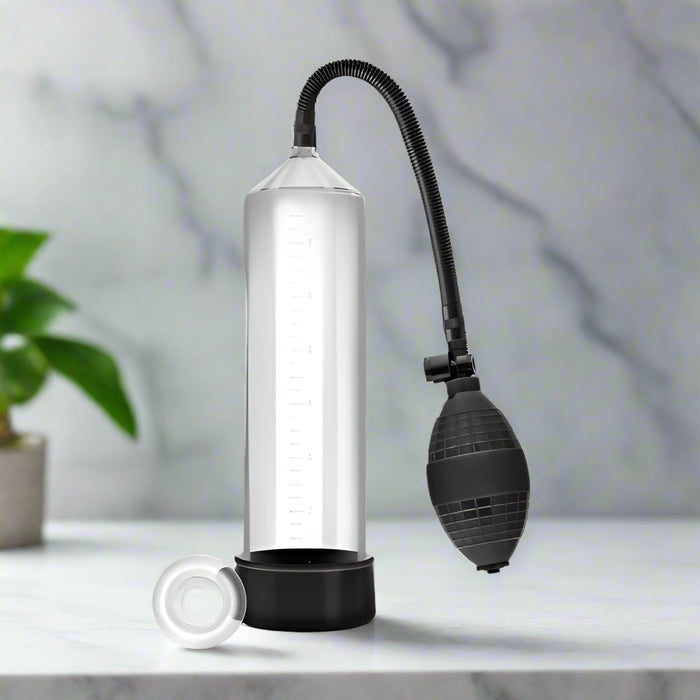 The Blush Performance Vx101 Male Enhancement Penis Pump is a transparent cylindrical pump that comes with a black base and a flexible hose ending in a black hand pump. It includes an additional Stay Hard Cock Ring accessory placed beside the pump, and the cylinder features a ruler on the side for measurement purposes.