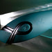 A close-up of the Pinpoint Perfection Flexible Slim Vibrator in teal shows its bendable, body-safe silicone surface with a power button and Playboy bunny logo, set against a blurred metallic background.