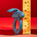 A Playboy Bunny Buzzer Vibrating Silicone Cock Ring in blue, made of body-safe silicone with rabbit ear extensions, stands upright by a yellow ruler (approx. 3 inches), set against a vivid red background.