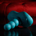 The Playboy Have a Seat Remote Control Grinding Vibrator Pad, a teal silicone personal massager with ribbed texture, rests on a glossy black surface before a red tufted background.