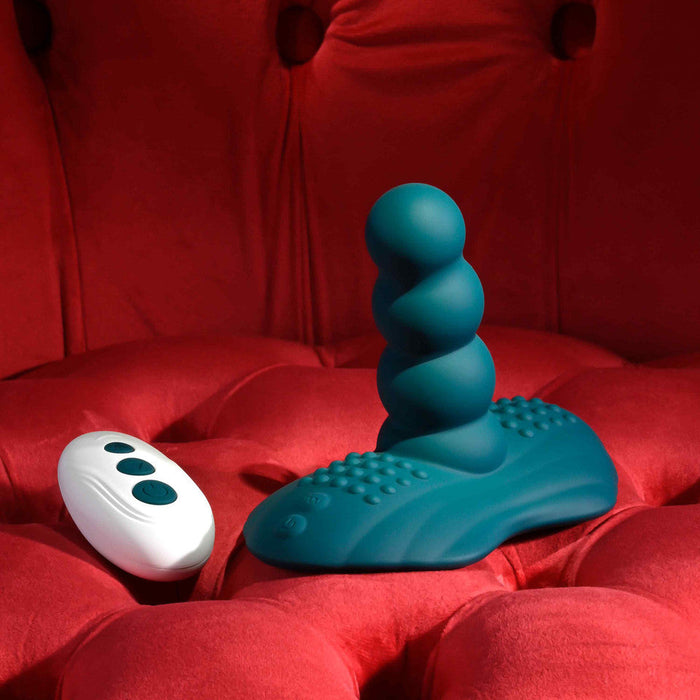 The Playboy Have a Seat Remote Control Grinding Vibrator Pad, in teal textured silicone with a suction cup base, rests on a tufted red velvet surface.