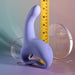 The Playboy Nice to Meet You Powerful Thrusting Vibrator with Handle stands upright in front of a yellow measuring tape. The background has two clear glass spheres and soft pastel color gradients.