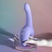 A pale mannequin hand holds the Playboy Nice to Meet You Powerful Thrusting Vibrator with Handle—lavender silicone, curved ergonomic design, and control buttons—displayed on glass against a soft pastel gradient background.