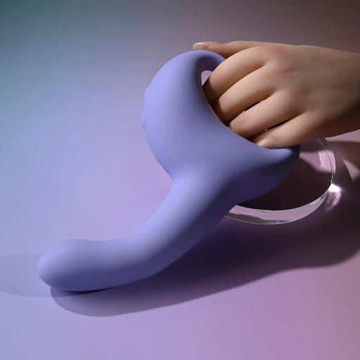 A hand holds the Playboy Nice to Meet You Powerful Thrusting Vibrator with Handle, a curved lavender silicone g-spot massager, against a softly lit gradient background of purple and blue.