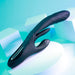 The Playboy Rapid Rabbit Thrusting Vibrator with Flapping Shaft, a sleek black personal massager with g-spot and dual-stimulation features, is set against a light turquoise background adorned with white geometric shapes.