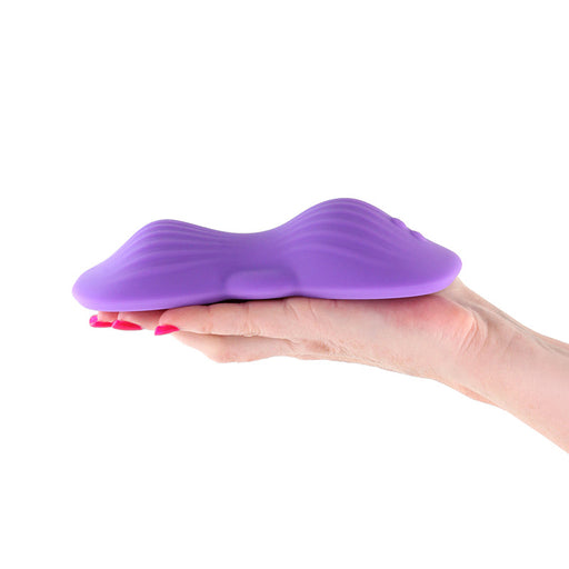 A hand with painted nails holds the Techno App-Controlled Hands-Free Grinding Pad, a purple, ridged, oval-shaped silicone device with a smooth ergonomic design, against a white background.
