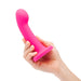 A hand holds the Pop Strap on Dildo & Harness Set in bright pink silicone, featuring a 5-inch curved design and flared base, ideal for solo play or use with a harness, set against a plain white background.