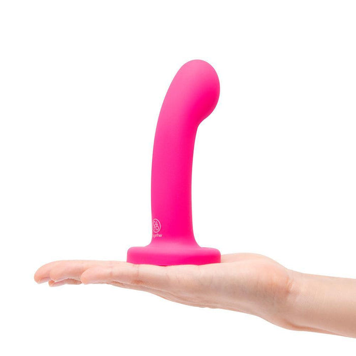 A hand holds the Pop Strap on Dildo & Harness Set in Pink Silicone—5 inches, featuring a curved shaft and flared base—against a white background.