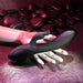 A black Rabbit Hole Double Ended G-Spot and Clitoral Suction Rabbit Vibrator from Evolved Novelties, crafted from premium silicone with a dual-prong design, rests on a pale mannequin hand. The background, featuring smooth dark stones and bathed in pink and purple lighting, creates a sensual atmosphere perfect for g-spot stimulation.