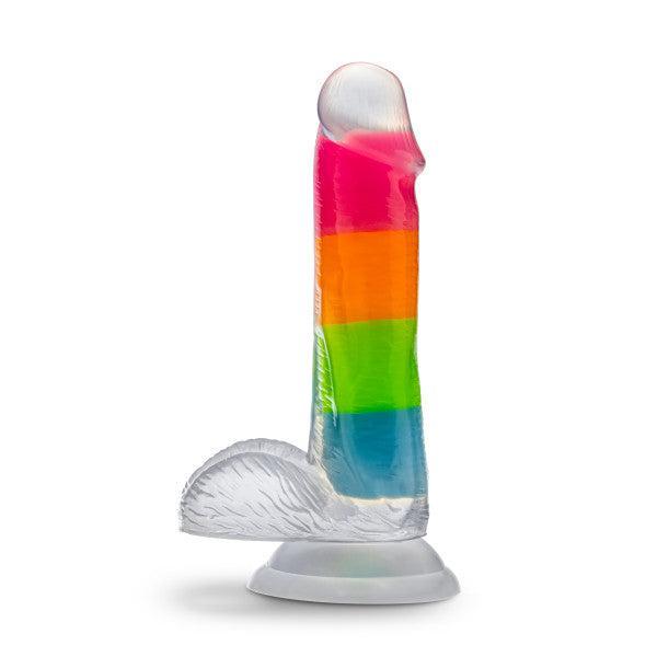 Introducing the Rainbow Rave Glow in the Dark 6.5 Inch Silicone Dildo by Blush, a vibrant and realistic-feeling translucent silicone toy with rainbow stripes. It features striking bands of pink, orange, green, and blue and includes a suction base for upright use against a plain white backdrop.