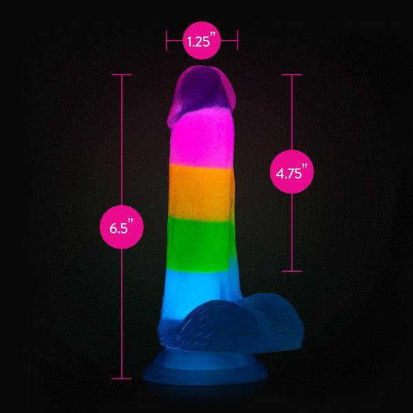 The Rainbow Rave Glow in the Dark 6.5 Inch Silicone Dildo by Blush stands upright against a black background, showcasing its colorful, striped design in neon shades of pink, orange, green, and blue. Pink circles highlight its dimensions: 6.5 inches tall, 1.25 inches wide, and 4.75 inches in circumference—offering a realistic feel for unique experiences.