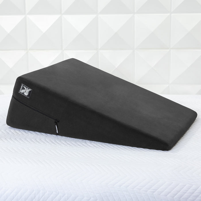 The Liberator Ramp Sex Positioning Cushion - 30 Inches in black, featuring a zippered cover, is placed on a white textured mattress against a geometric-patterned wall.