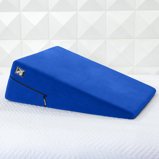 A Liberator Ramp Sex Positioning Cushion - 30 Inches in blue with a zippered cover rests on a white quilted surface, set against a white geometric tiled wall.