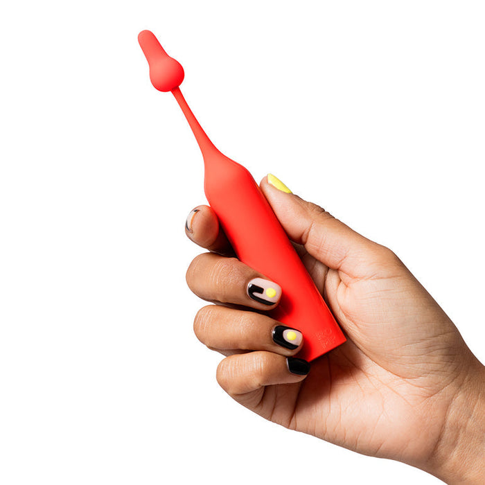 A hand with painted nails holds the Romp Pop Pinpoint Clitoral Stimulator with 2 Heads, featuring a bright red rounded tip, against a plain white background.