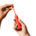 A person with yellow and black painted nails holds a red Romp Pop Pinpoint Clitoral Stimulator with 2 heads in one hand and a small red ball in the other, against a white background.