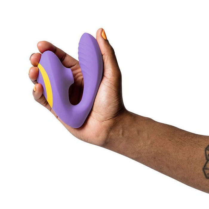 A hand holds the Romp Reverb Pleasure Air Vibrator for G-Spot & Clitoris, shown in purple and yellow against a white background.