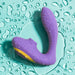 The Romp Reverb Pleasure Air Vibrator for G-Spot & Clitoris, in purple and yellow with a curved waterproof design, rests on a teal surface with water droplets, ready to provide intense stimulation.
