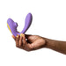 A hand with painted nails holds the Romp Reverb Pleasure Air Vibrator for G-Spot & Clitoris in purple and yellow against a white background.