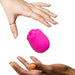 Two hands, one light and one dark-skinned, cradle the Romp Rose 2 Pleasure Air Clitoris Stimulator—a small, pink, rose-shaped silicone toy—against a white background.