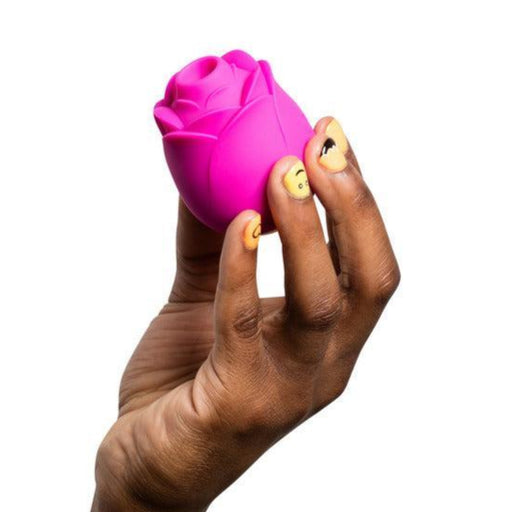 A hand with painted nails holds a small, pink, rose-shaped object against a white background—the Romp Rose Pleasure Air Clitoris Stimulator by WOW, designed to harness Pleasure Air Technology for an unparalleled experience.