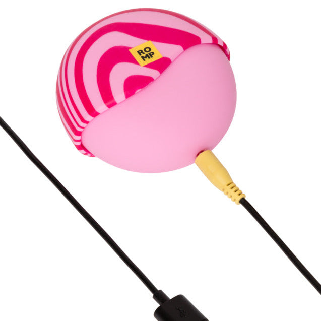 The Romp Spin Small Discreet Pleasure Air Clitoral Stimulator is a pink, oval-shaped travel-size vibrator with magenta stripes, a yellow "ROMP" label, and comes with a yellow cable and black USB charging cord.