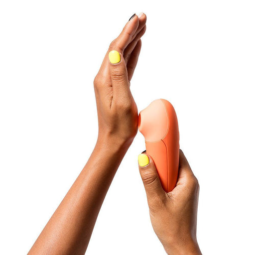 A person with yellow-painted nails holds an orange Romp Switch X Beginner's Pleasure Air Clitoral Stimulator by WOW against the palm of their other hand. The sleek and ergonomic device features Pleasure Air Technology, perfect for a blissful experience.