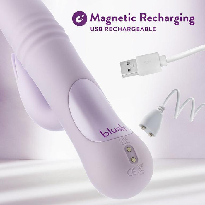 A purple Rylee Clit Fluttering G-Spot Thrusting Rabbit from Blush, featuring charging icons, lies beside a USB charging cable and a magnetic charging head. The text "Magnetic Recharging USB Rechargeable" is at the top, emphasizing its versatility for clitoral massaging. The background is a soft, out-of-focus light purple.