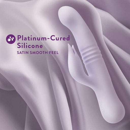 An image displaying the Blush Rylee Clit Fluttering G-Spot Thrusting Rabbit, crafted from platinum-cured silicone for a satin-smooth feel. The light purple vibrator boasts a sleek, ergonomic design with textured elements and an attached stimulator for clitoral massaging. Text on the image reads: "Platinum-Cured Silicone. Satin Smooth Feel.
